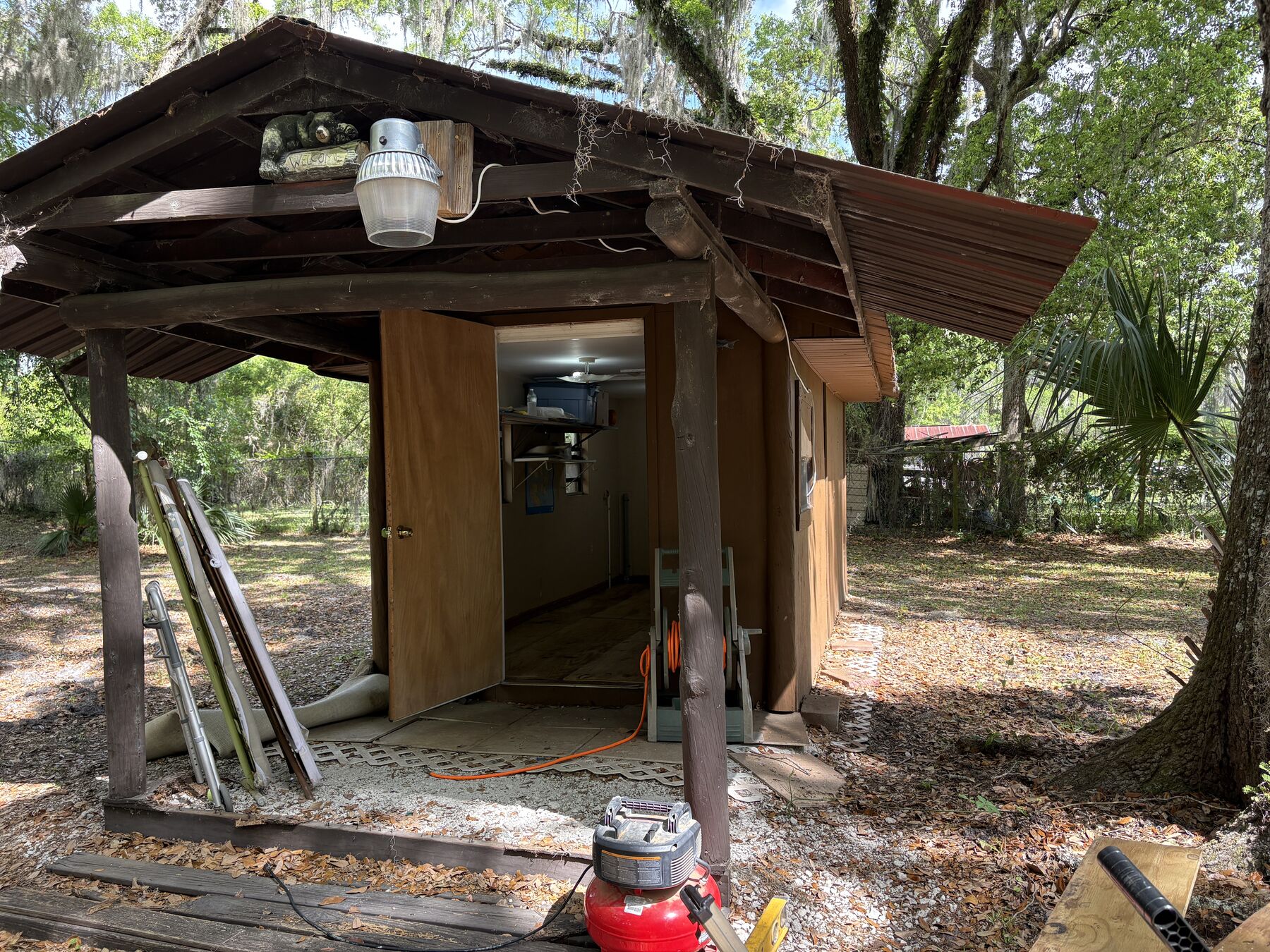 The building: a deep covered porch on rough posts, pitched metal roof, open door, live oaks and Spanish moss